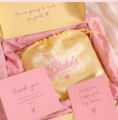 Blake’s Bundles box opened: pink tissue, a butter-yellow satin drawstring bag and two pink cards